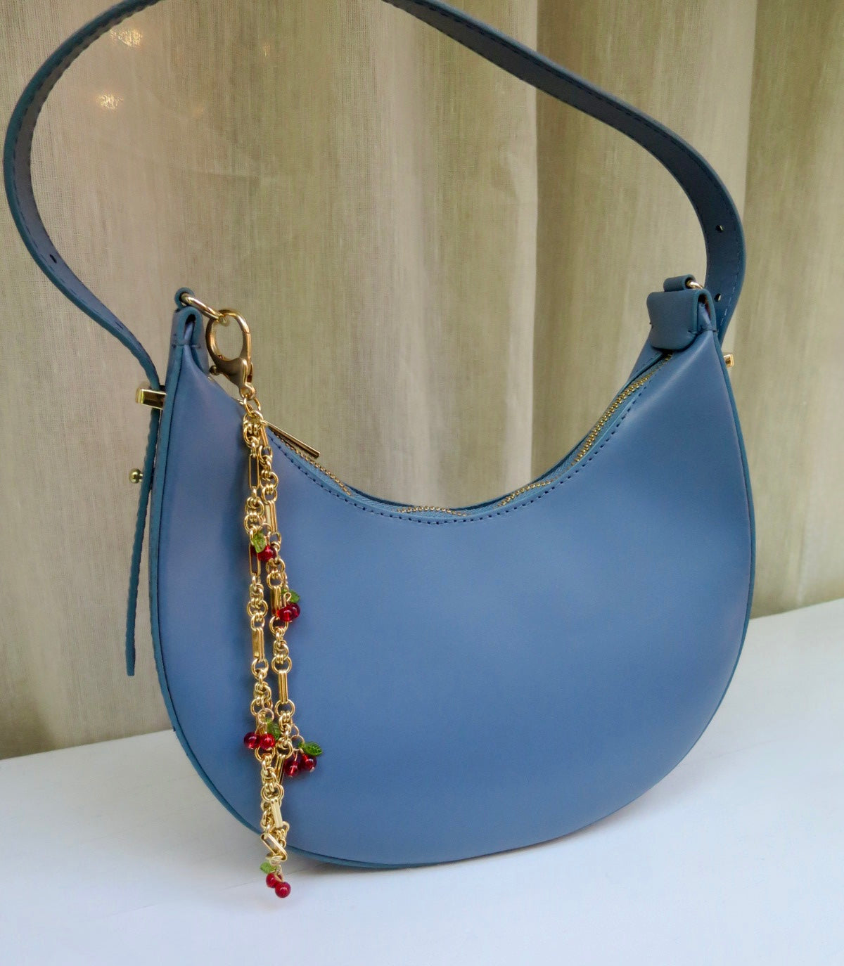 Blue handbag with a decorative chain strap on a neutral background
