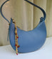 Blue handbag with a decorative chain strap on a neutral background
