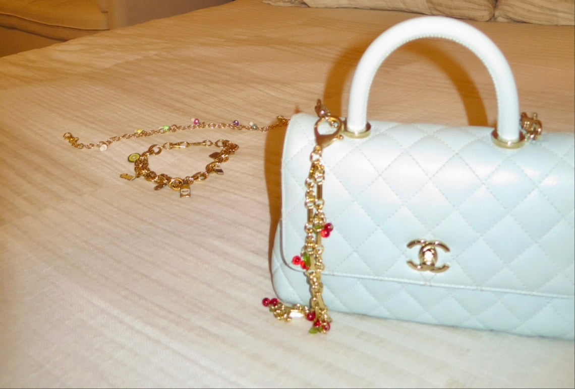 White quilted handbag with gold chain and red beads on a beige surface